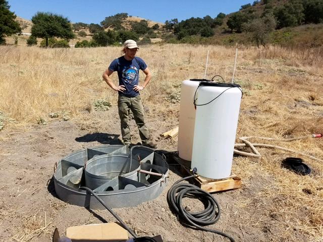 USGS hydrologist standing in a field overlooking an infiltrometer and other equipment.