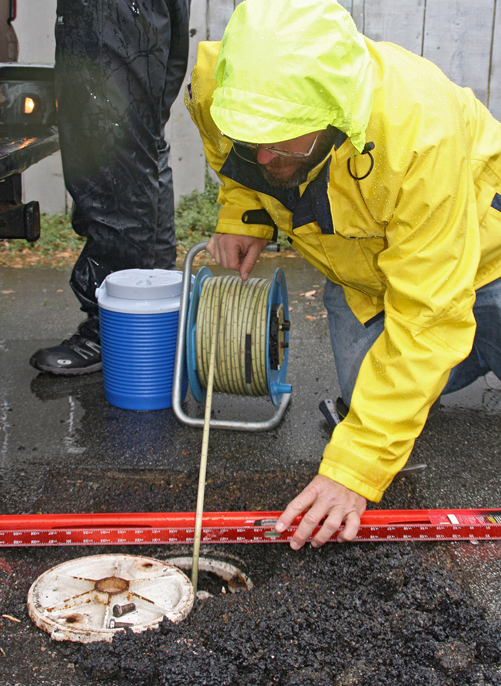 Photo of a USGS hydrologist conducting a manual water-level measurement by dropping a specialized tape measure into a well.